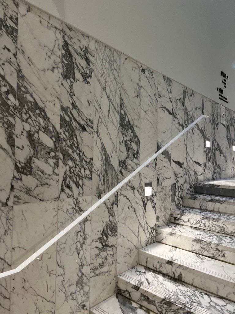 Escalier en marbre blanc fortement veiné, le mur habillé de la même pierre